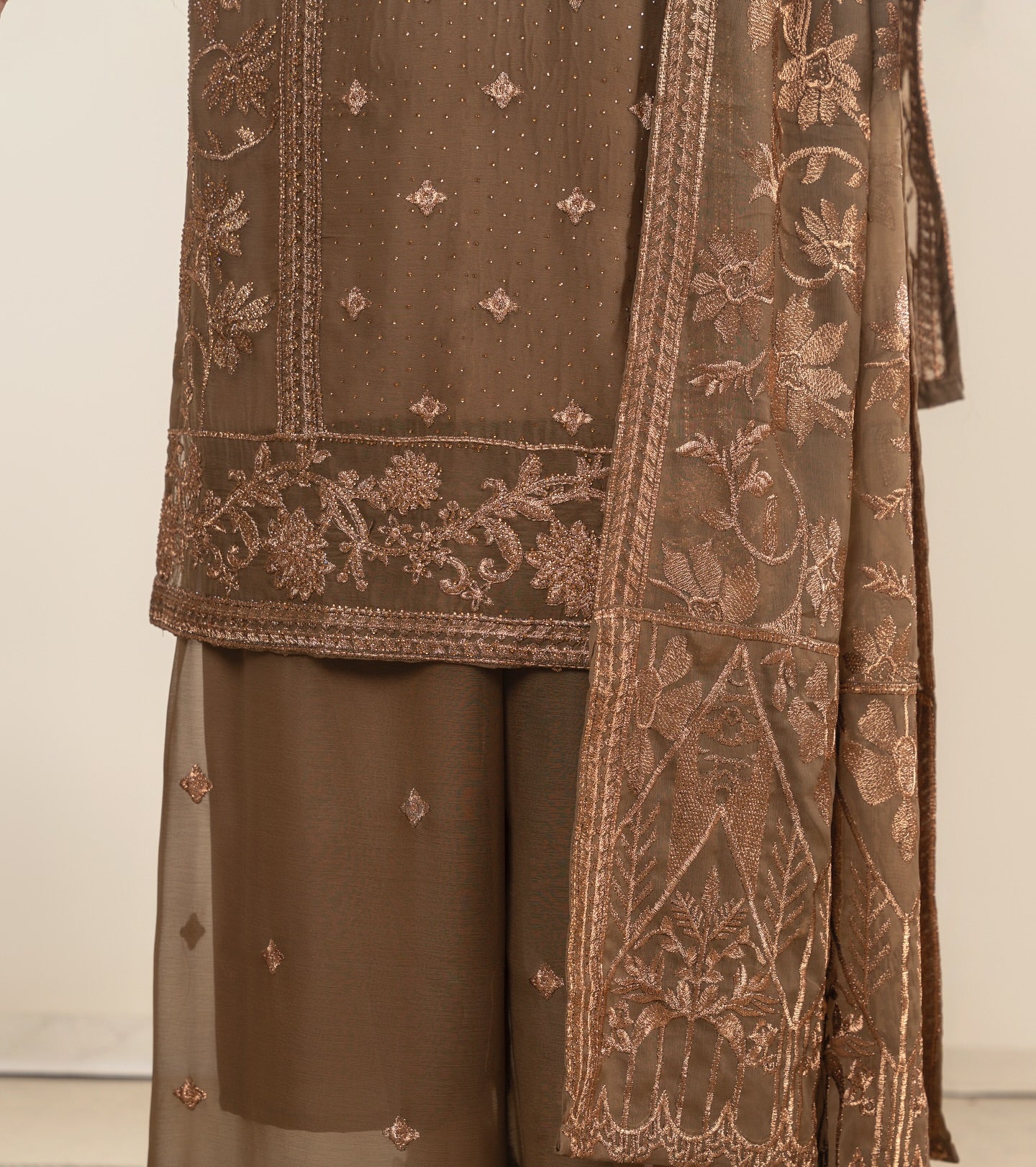 Brown embroidered traditional outfit with a sheer dupatta on a plain background