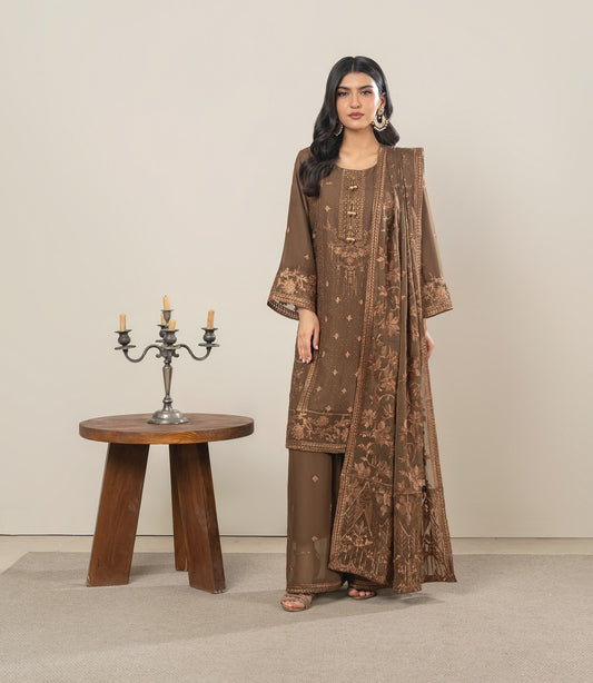 Woman in a brown embroidered outfit standing next to a wooden table with a candle holder.