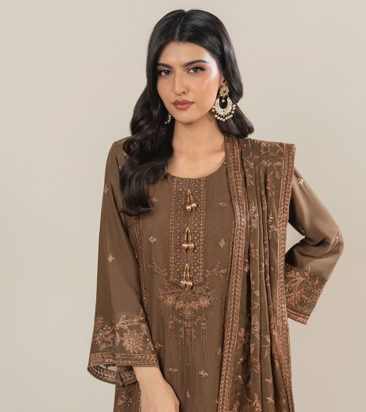 Woman wearing a brown embroidered outfit against a plain background