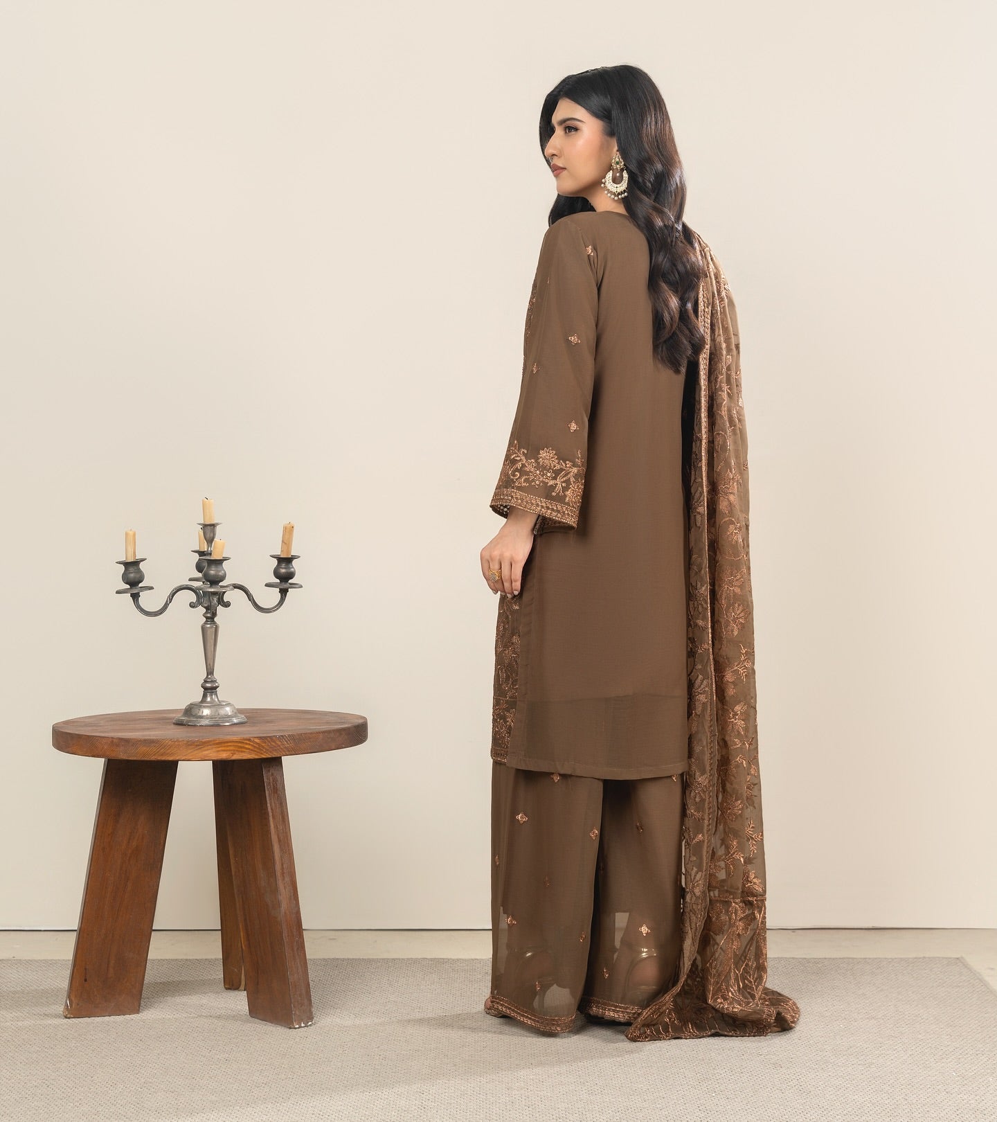 Woman in a brown traditional outfit standing next to a wooden table with a candle holder.